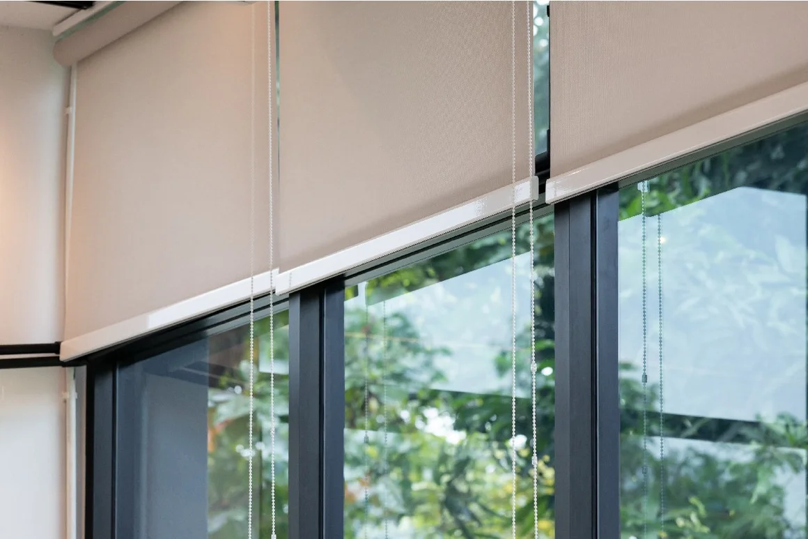 Beige Rollos vor einem Fenster mit Blick ins Grüne